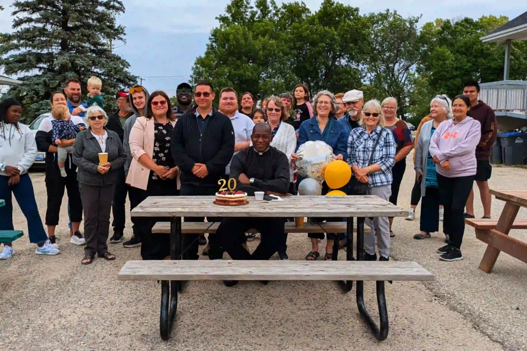 father sebastian at picnic table with cake. parish behind him.