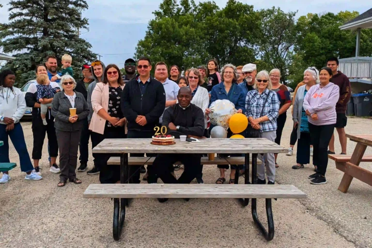 father sebastian at picnic table with cake. parish behind him.